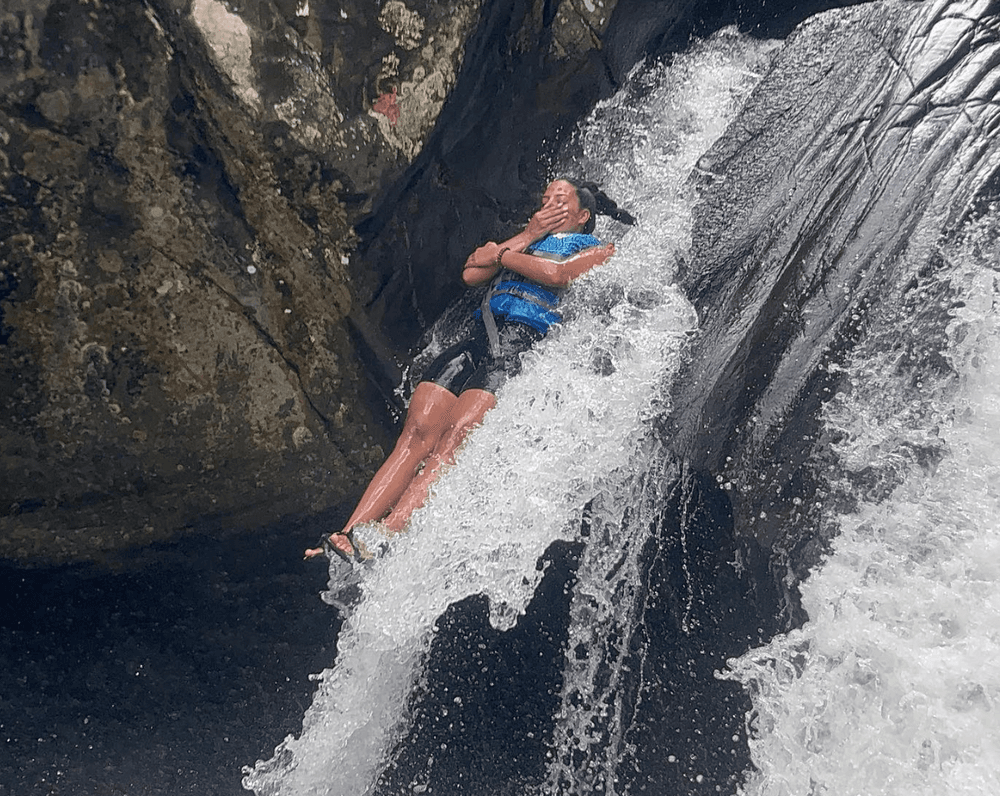 Adventurer sliding down natural waterfall in a rocky gorge