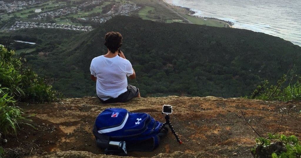Solo hiker seated on cliff overlooking coastal valley and ocean view