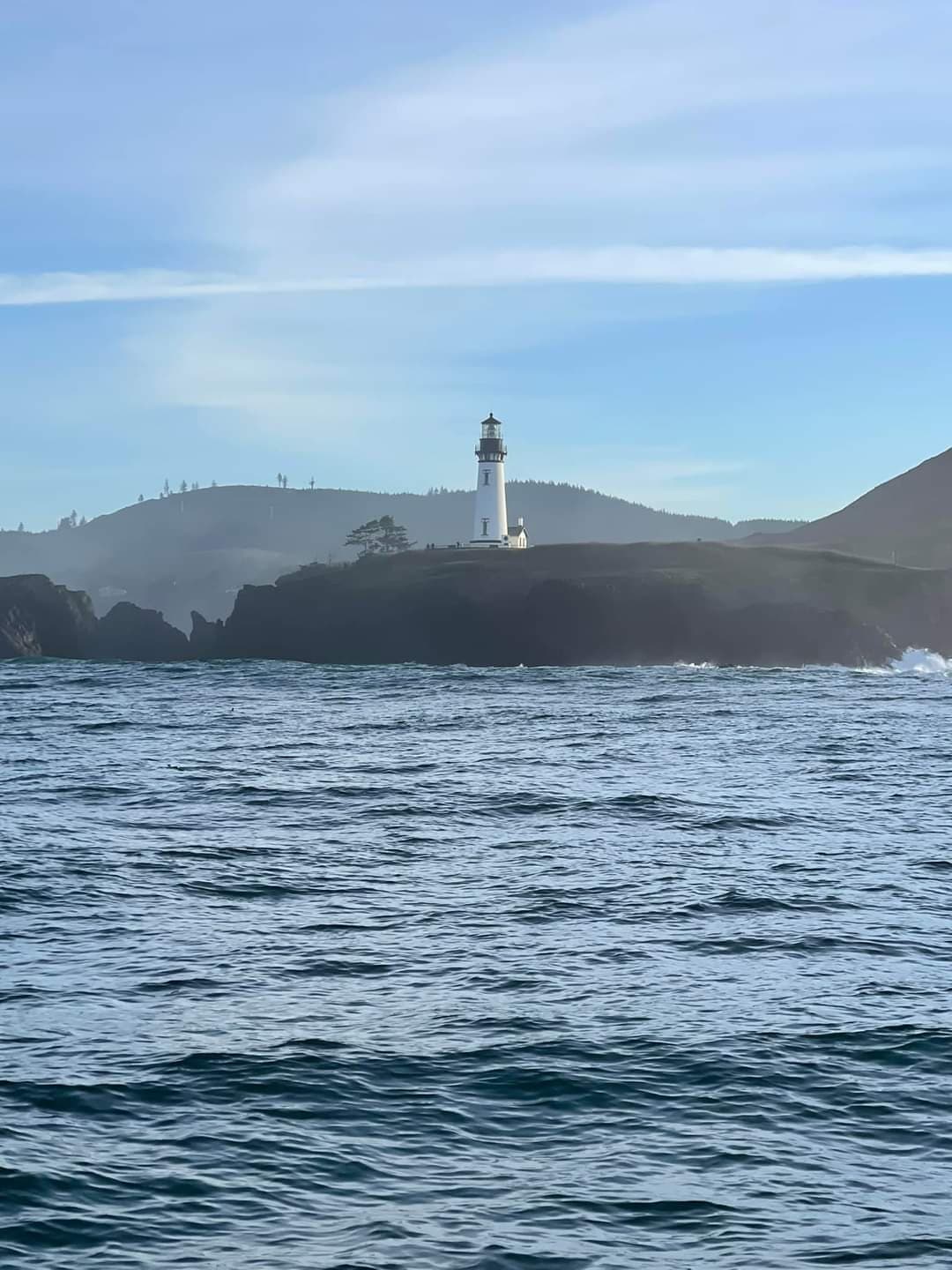 Lighthouse on rocky headland over Yaquina Bay, ocean charter backdrop