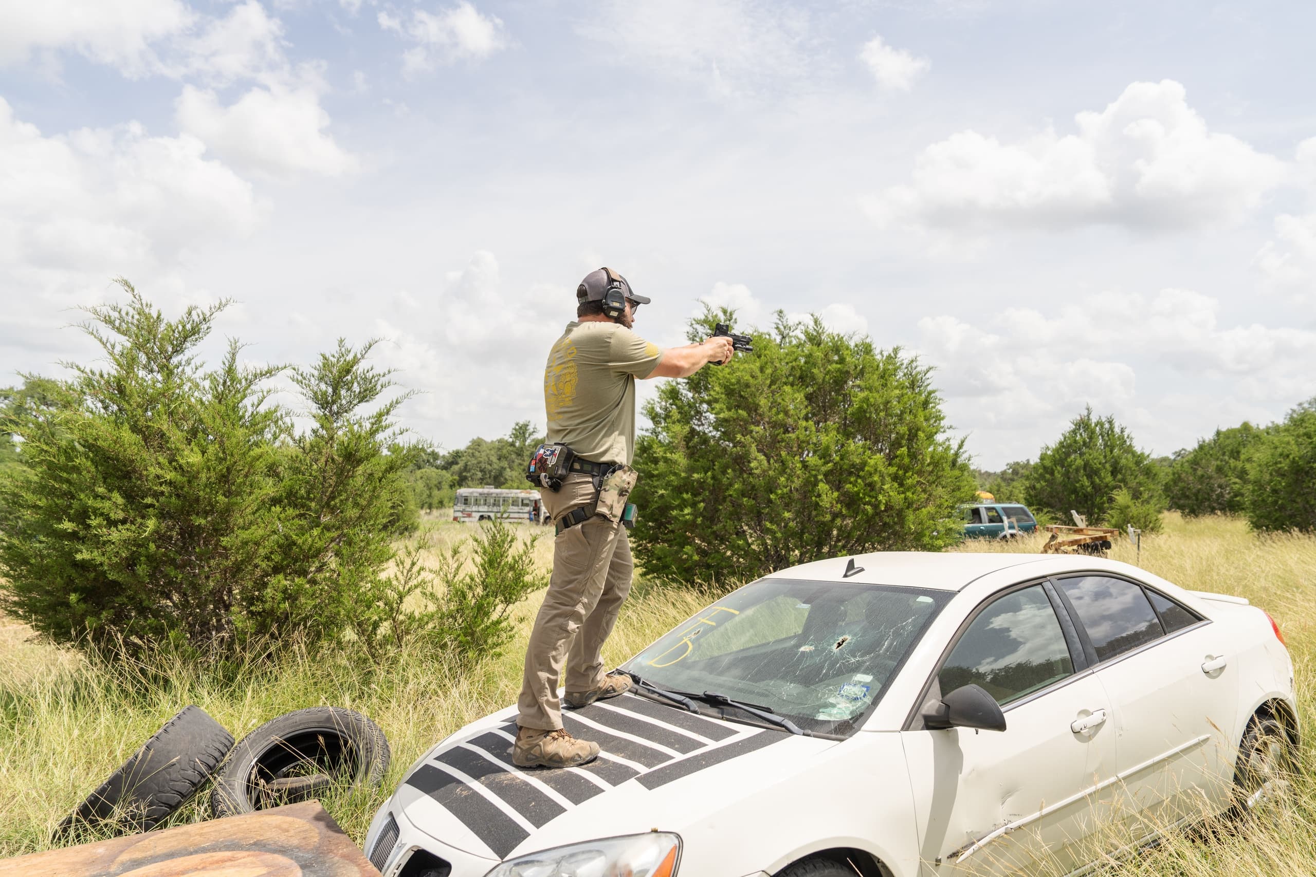 Shooter practicing tactical shooting on car in grassy range