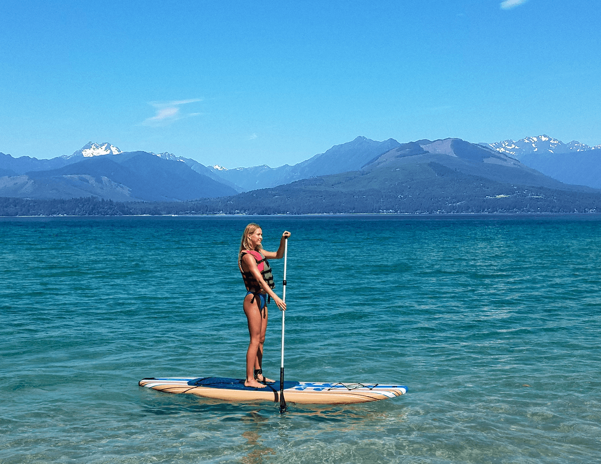 Paddleboarder on crystal blue water with mountain range horizon
