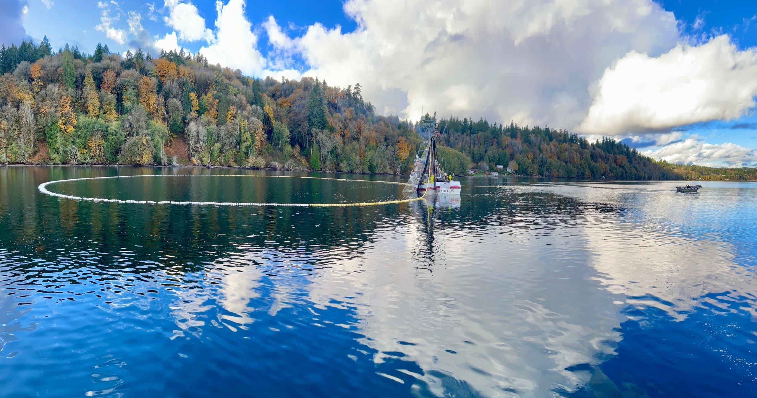Person on small sailboat cruising a reflective lake with autumn trees