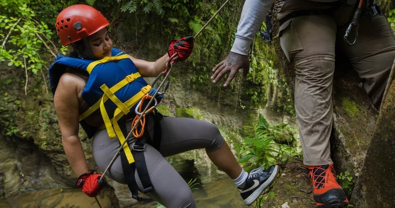 Woman descending canyon rappel in forested gorge with guide