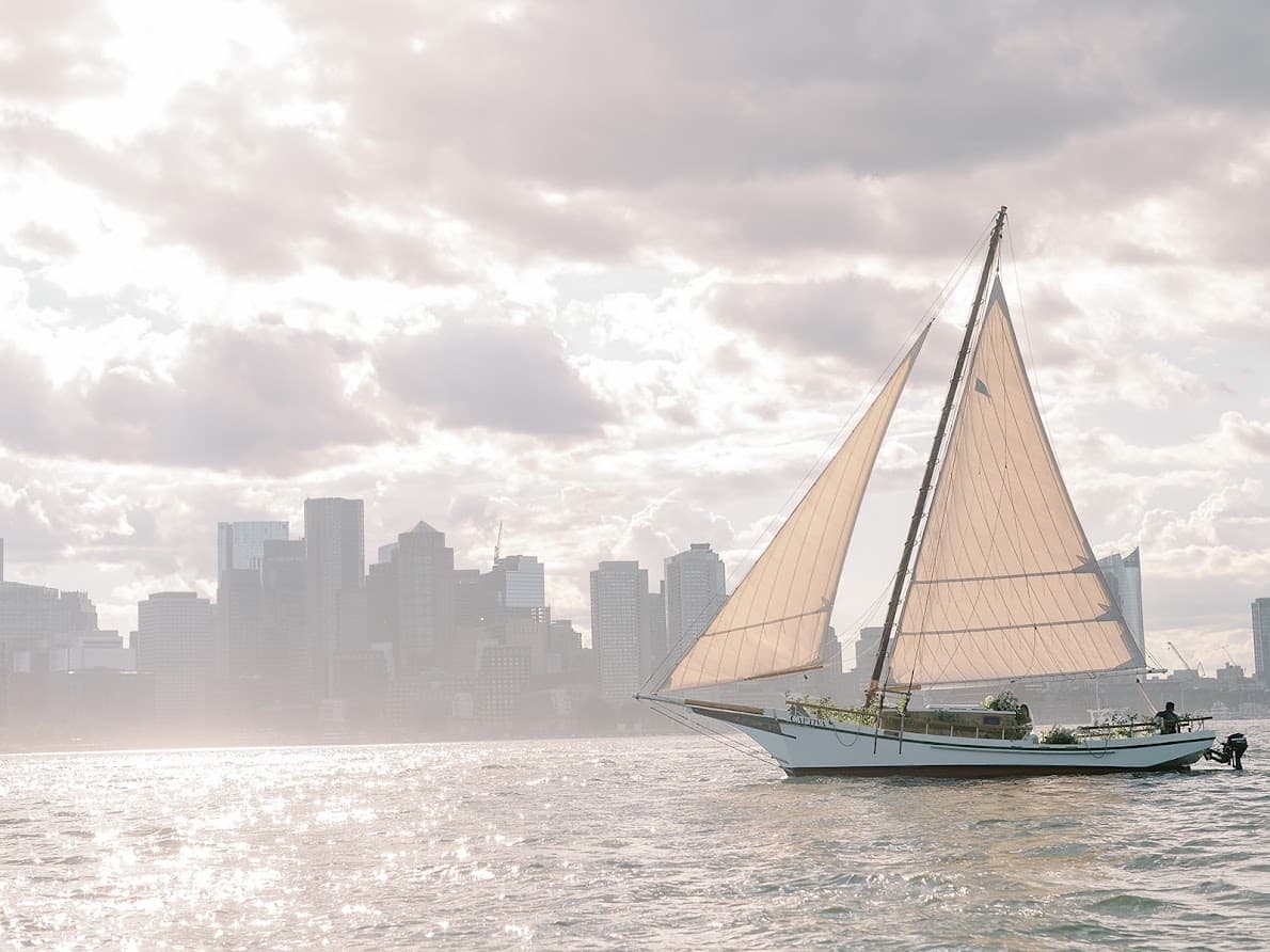 Sailboat cruising past Boston Harbor skyline on sunny afternoon