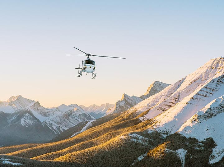 Helicopter flying over snow-capped mountain range at sunrise