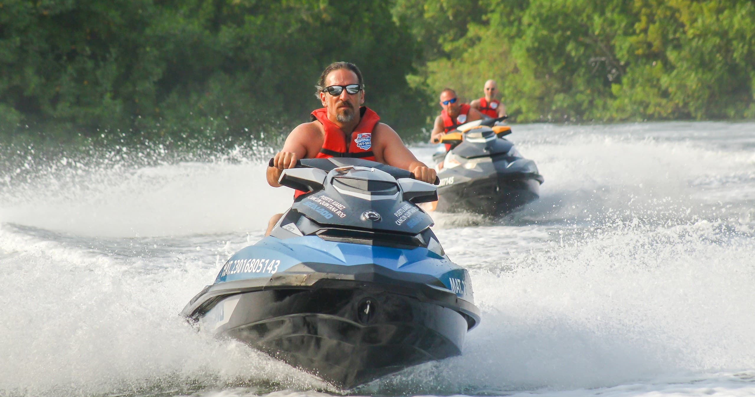 Jet ski riders speeding across tropical bay with wake spray