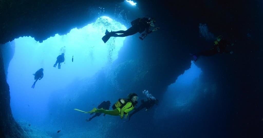 Group of scuba divers under rocky arch in clear Atlantic waters