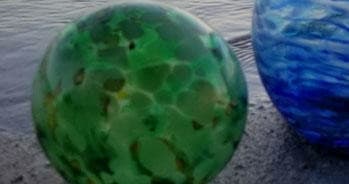 Green blown-glass orb photographed near ocean shoreline in Hawaii