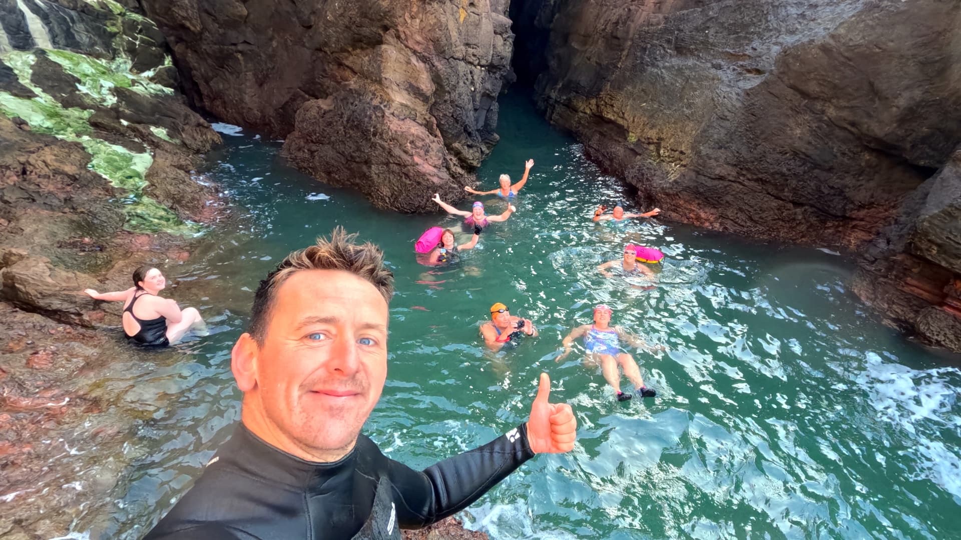 Group cliff swimmers enjoying rocky sea pool with guide selfie