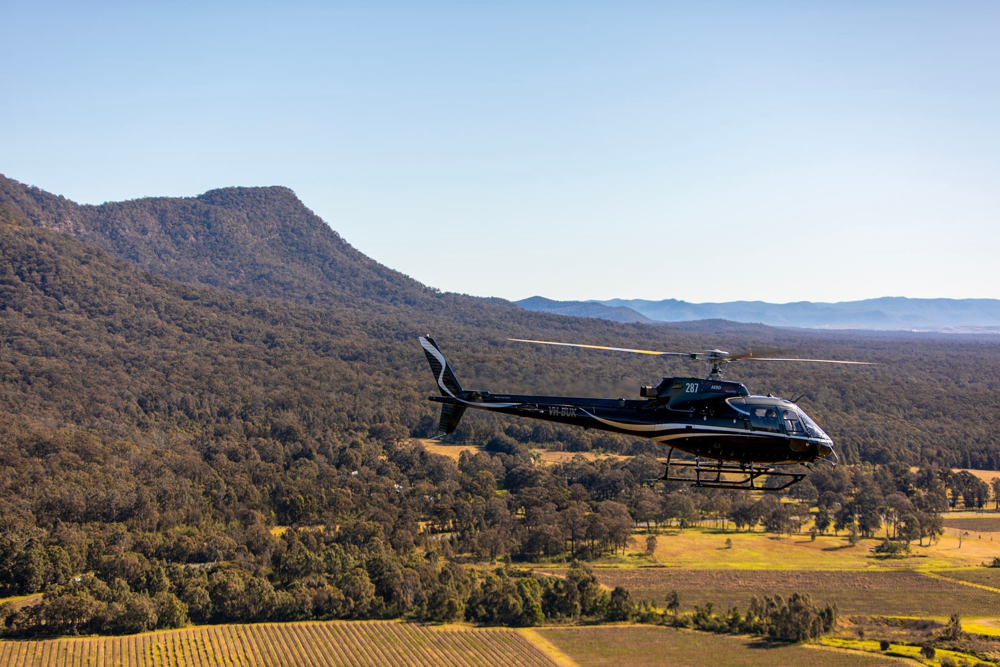 Helicopter flying over vineyard valleys toward distant mountains