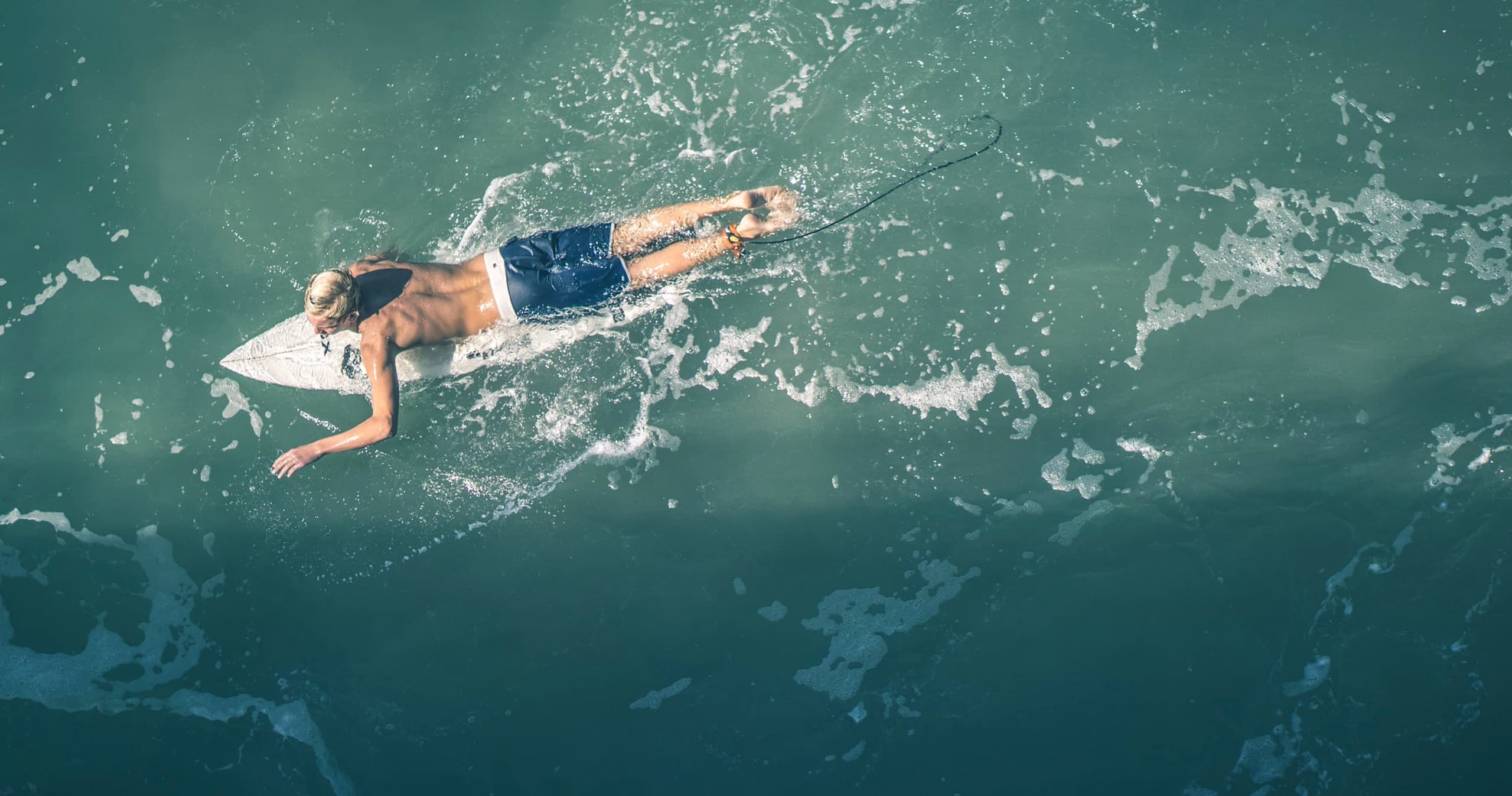 Surfer paddling on a surfboard through turquoise open ocean waves