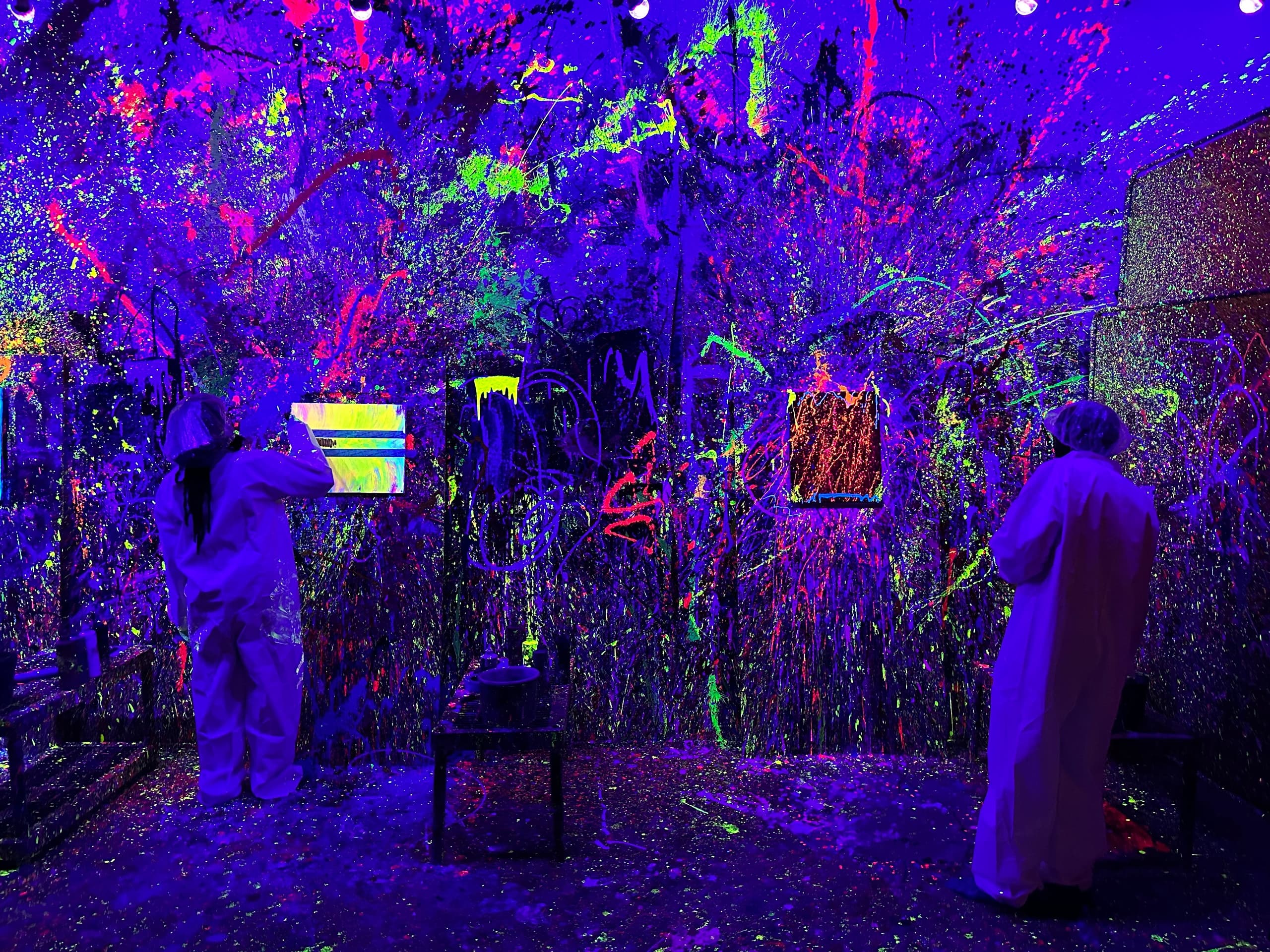Artists splattering neon paint in immersive blacklight studio