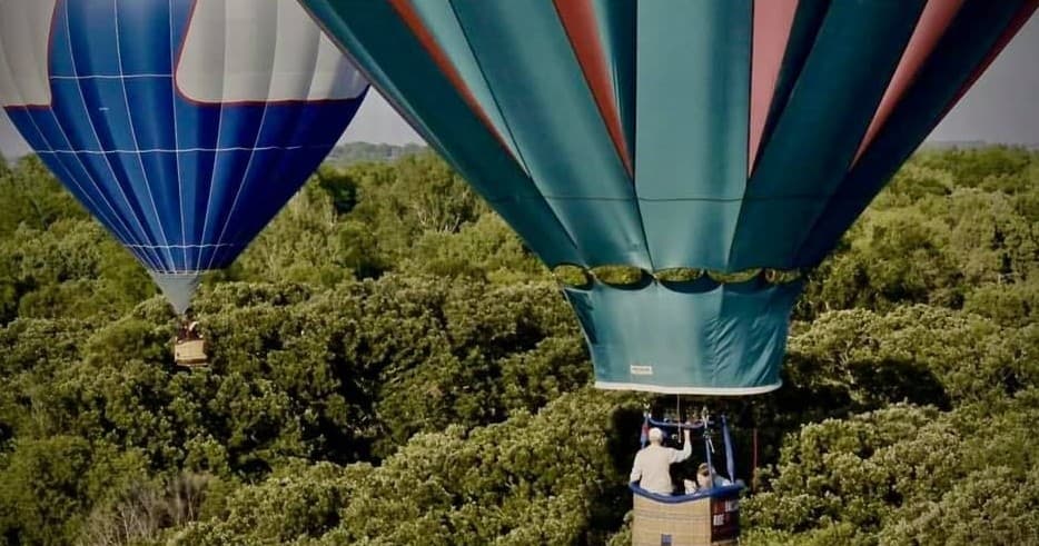 Close-up hot air balloons with passengers drifting above green forest