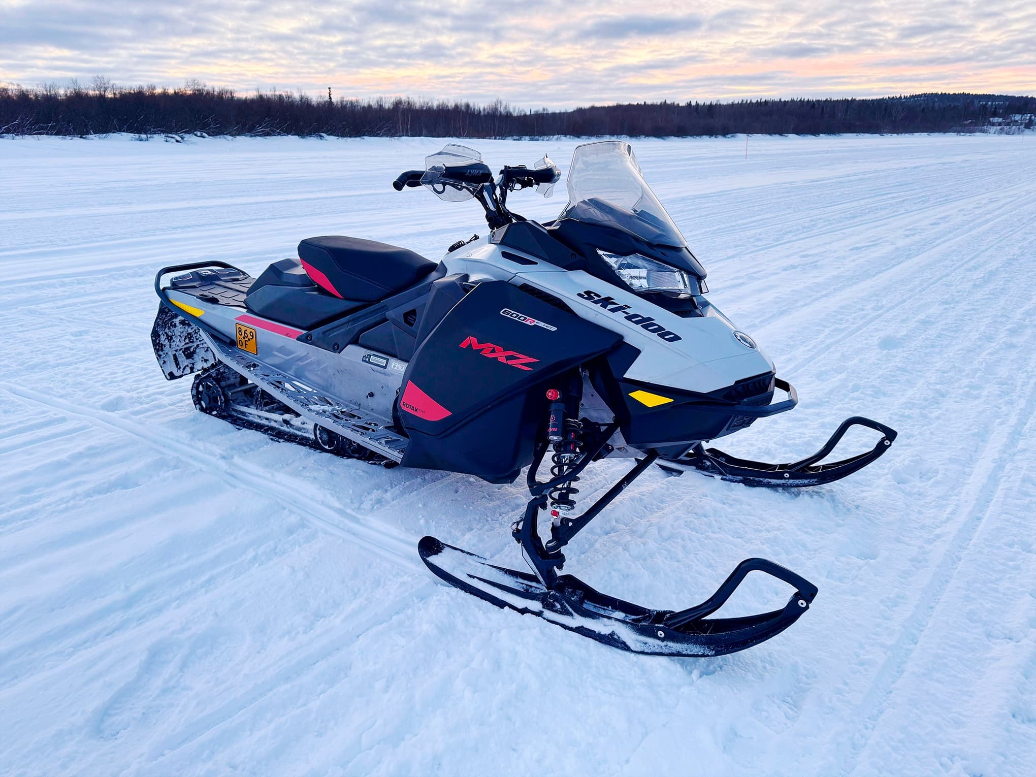 Snowmobile parked on frozen lake at sunset in boreal landscape