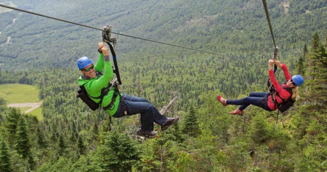 Two people ziplining over alpine forest canopy in mountain valley
