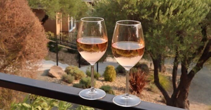 Two wine glasses on balcony overlooking trees at sunset