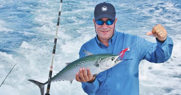 Angler holding caught pelagic fish on deck against ocean spray
