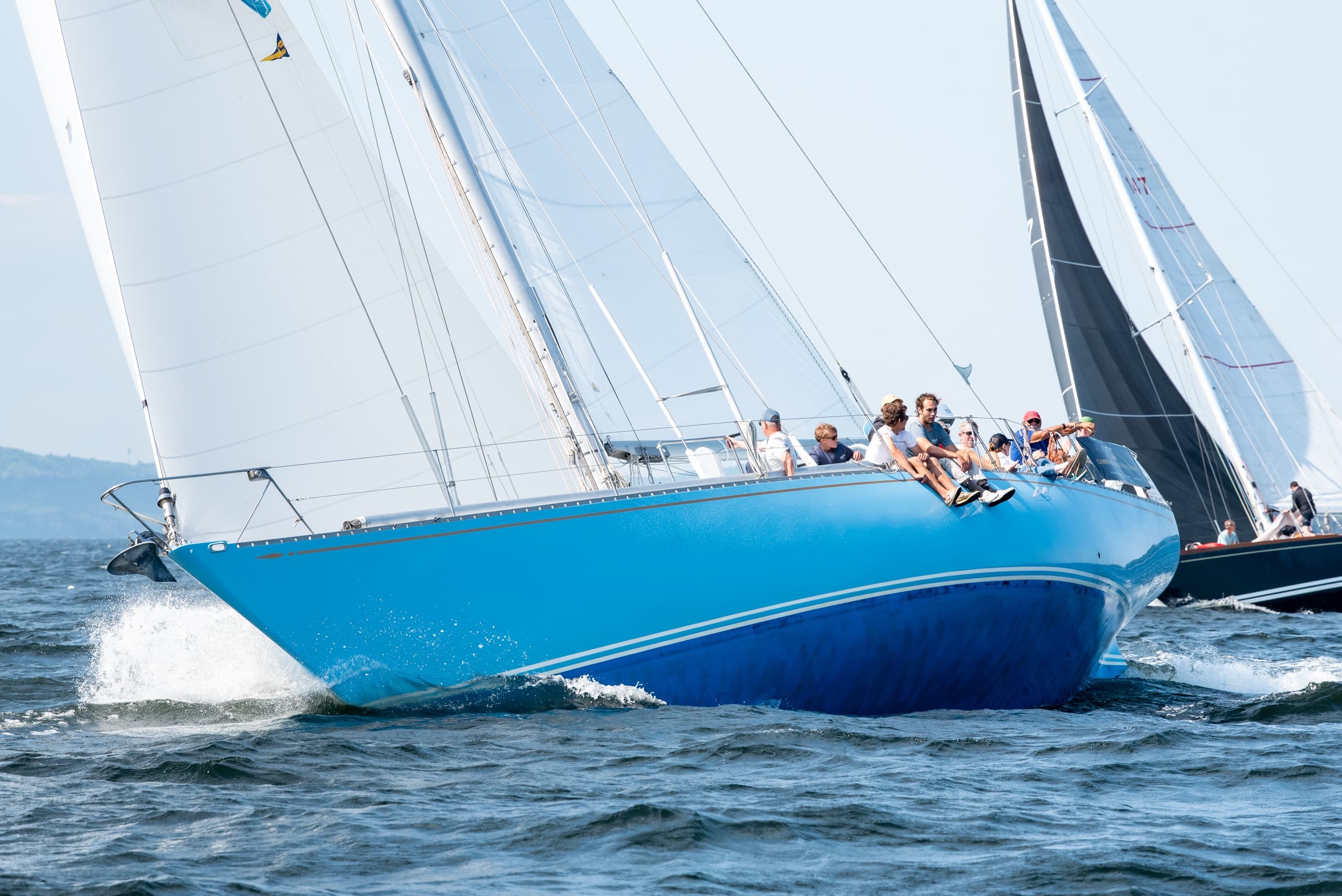 Blue racing sailboat heeling sharply with crew in windy ocean