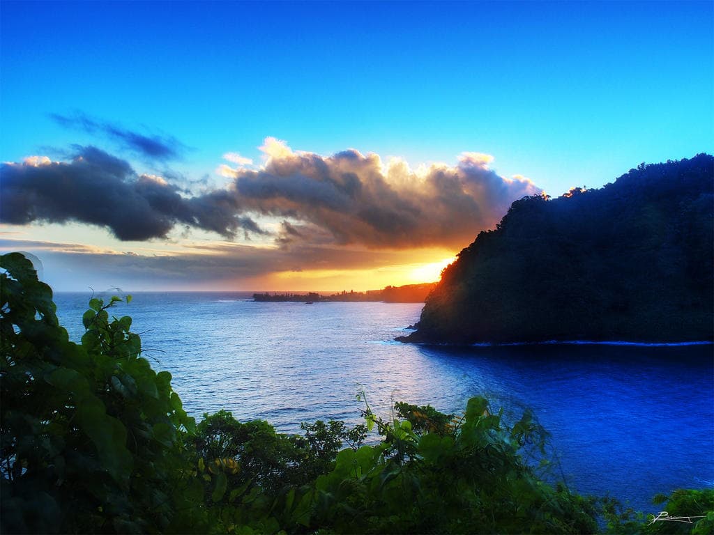 Sunset over serene bay with silhouetted coastal cliffs