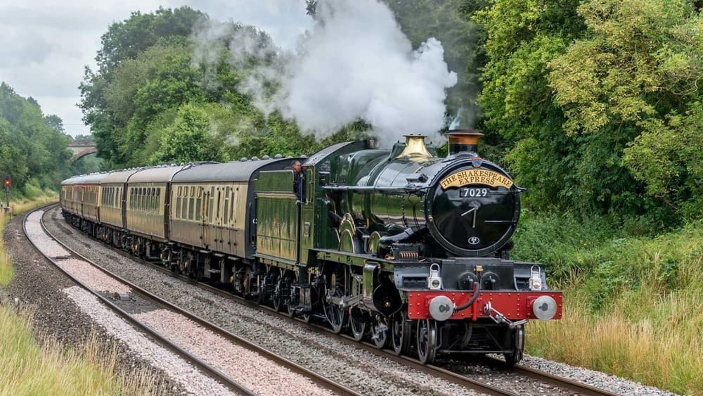 Classic steam locomotive hauling heritage carriages through leafy fields