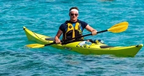 Solo kayaker paddling turquoise coastal waters near shoreline