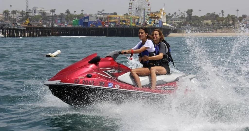 Two riders on a red jet ski splashing near Marina del Rey pier