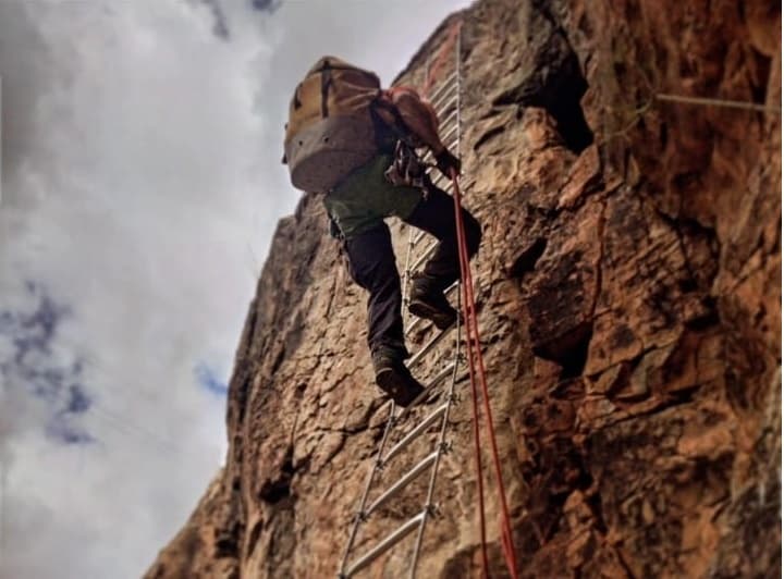 Rock climber ascending ladder on steep cliff face, technical climb