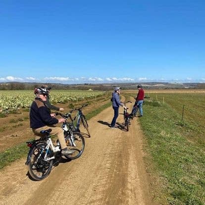 Cyclists riding dirt trail across open coastal fields at sunrise