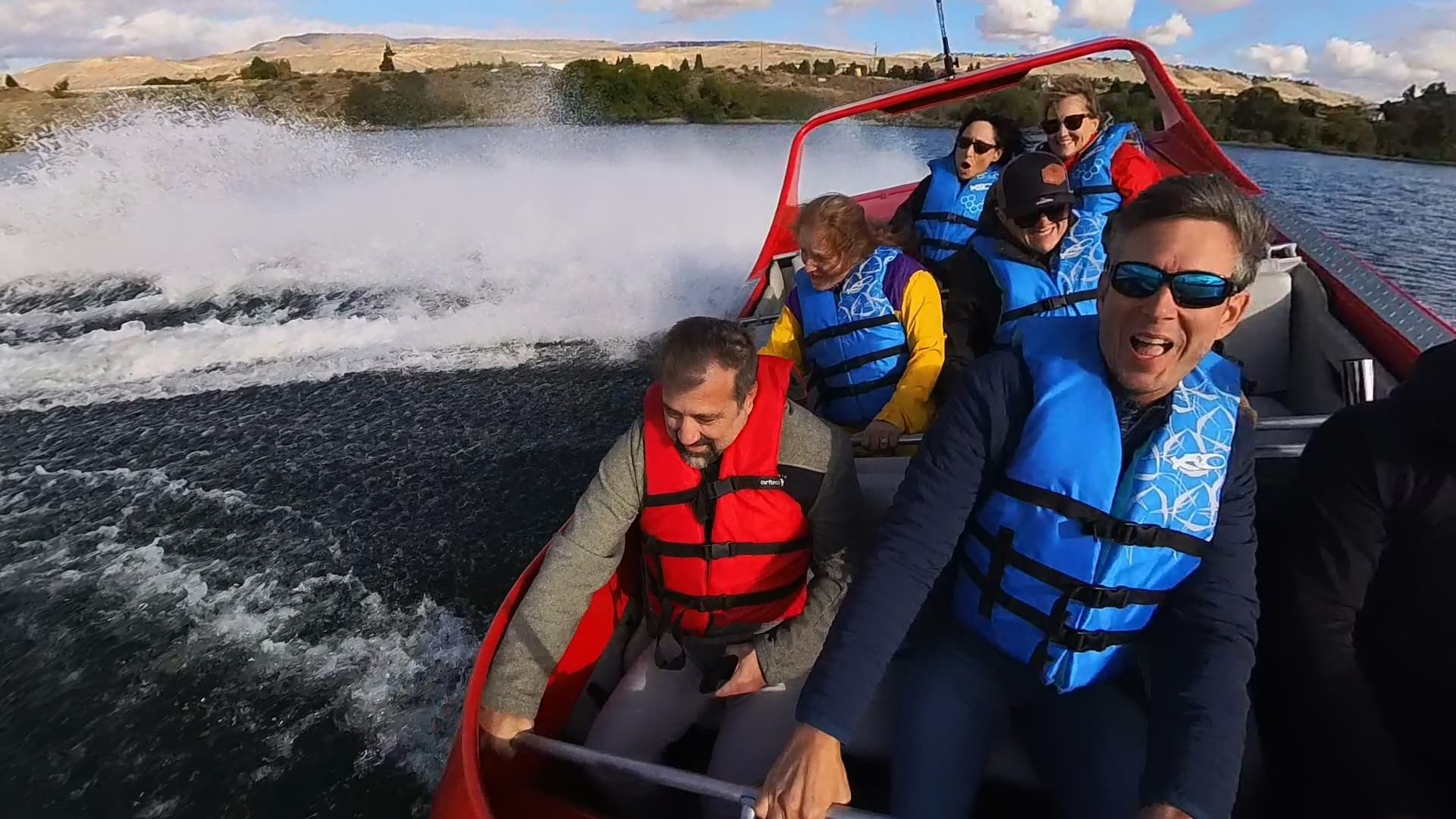 Group gripping rails in jet boat creating dramatic wake on river