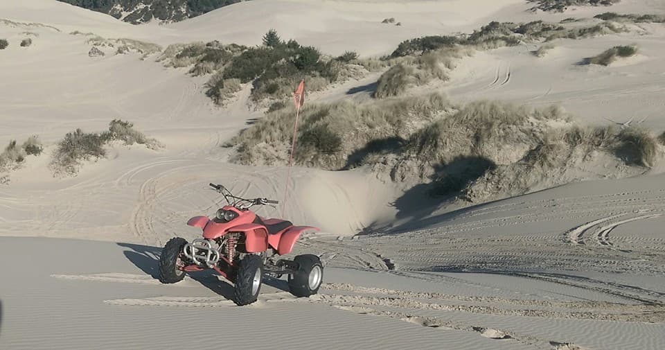 Red quad riding across steep sand dunes for off-road adventure