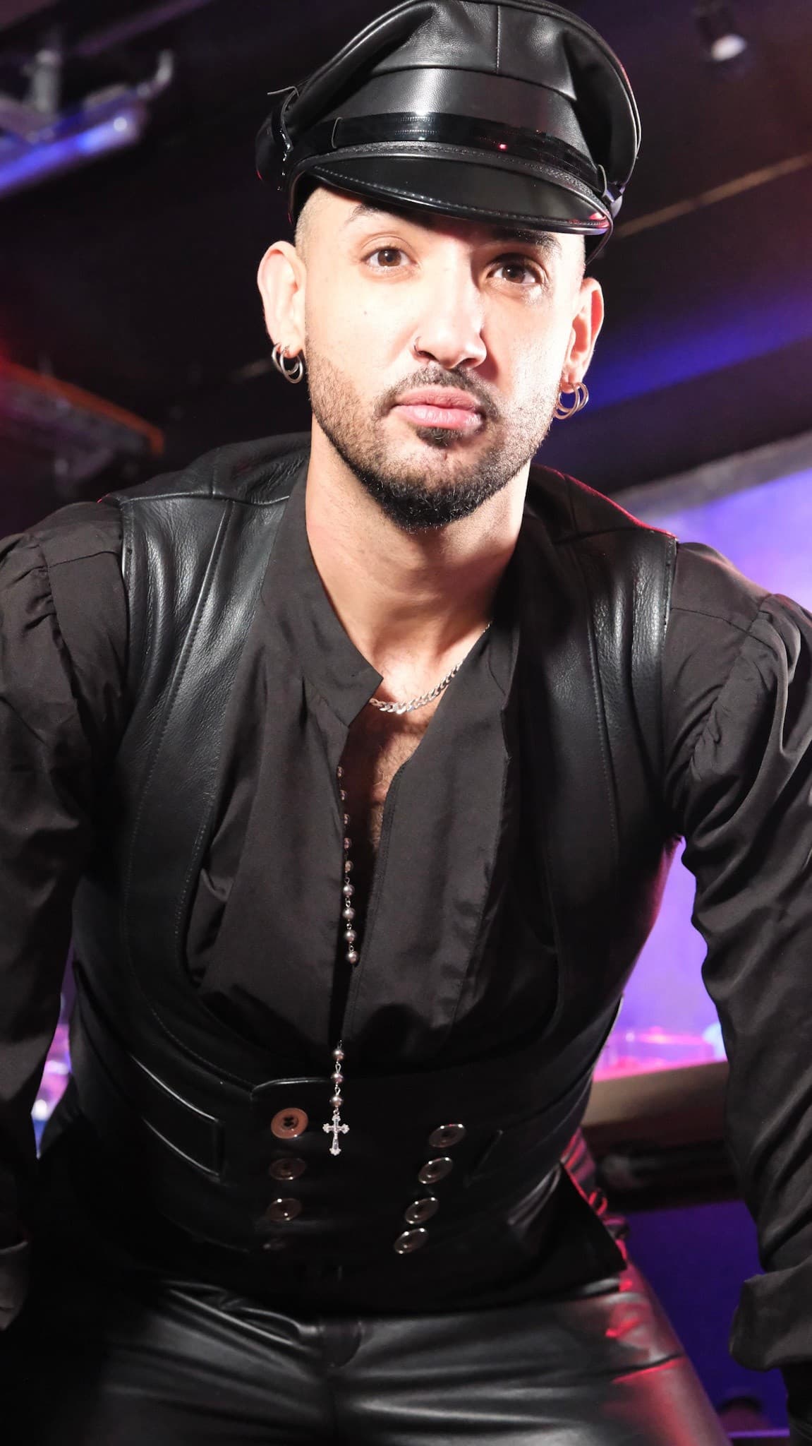 Man in leather outfit and cap posing in nightclub interior