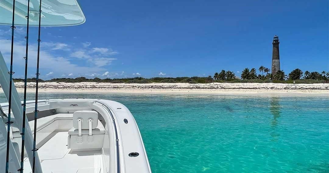 Boat bow with turquoise water and lighthouse on island shore