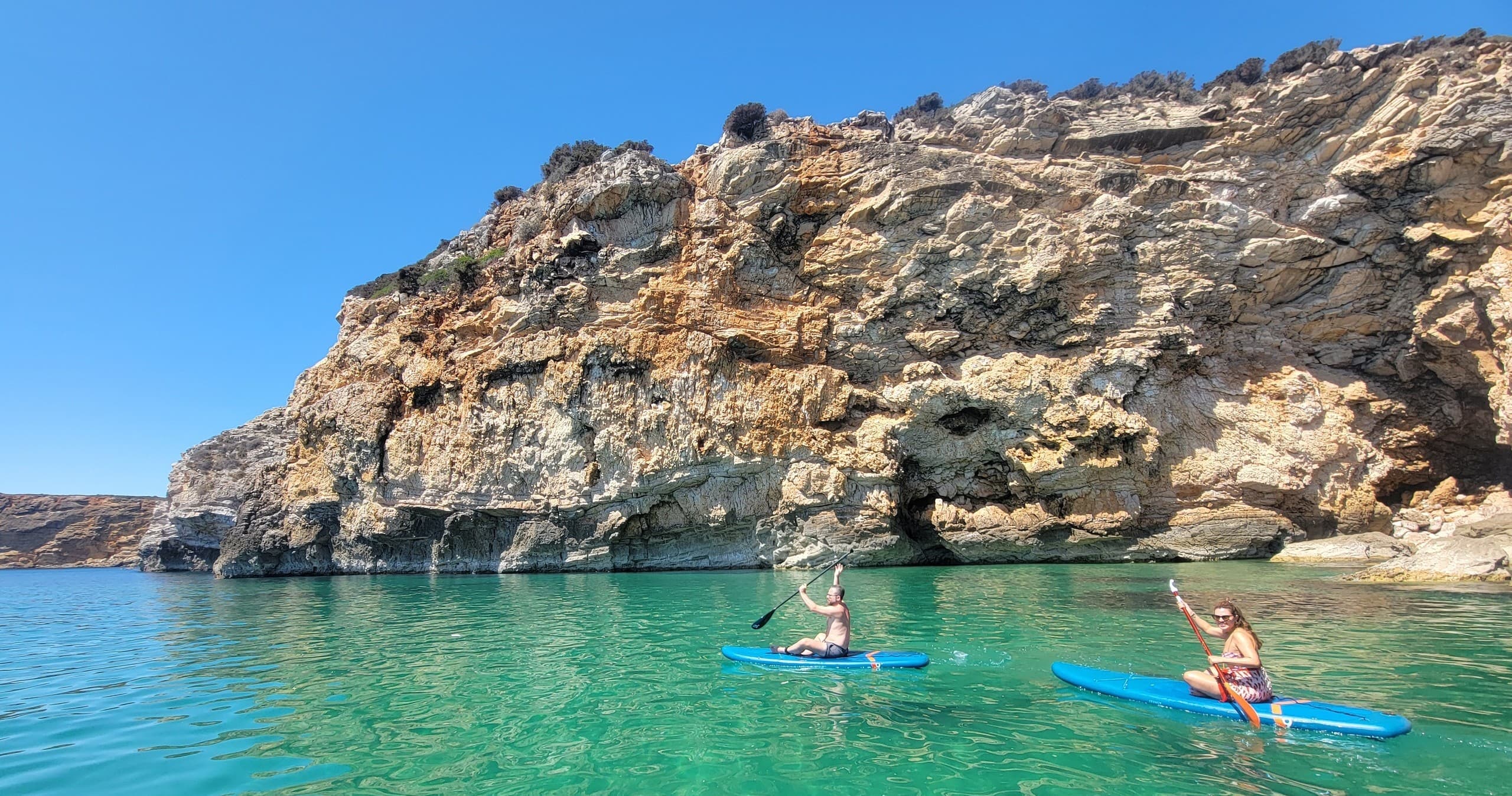 Paddleboarders exploring clear water beside rugged cliffs
