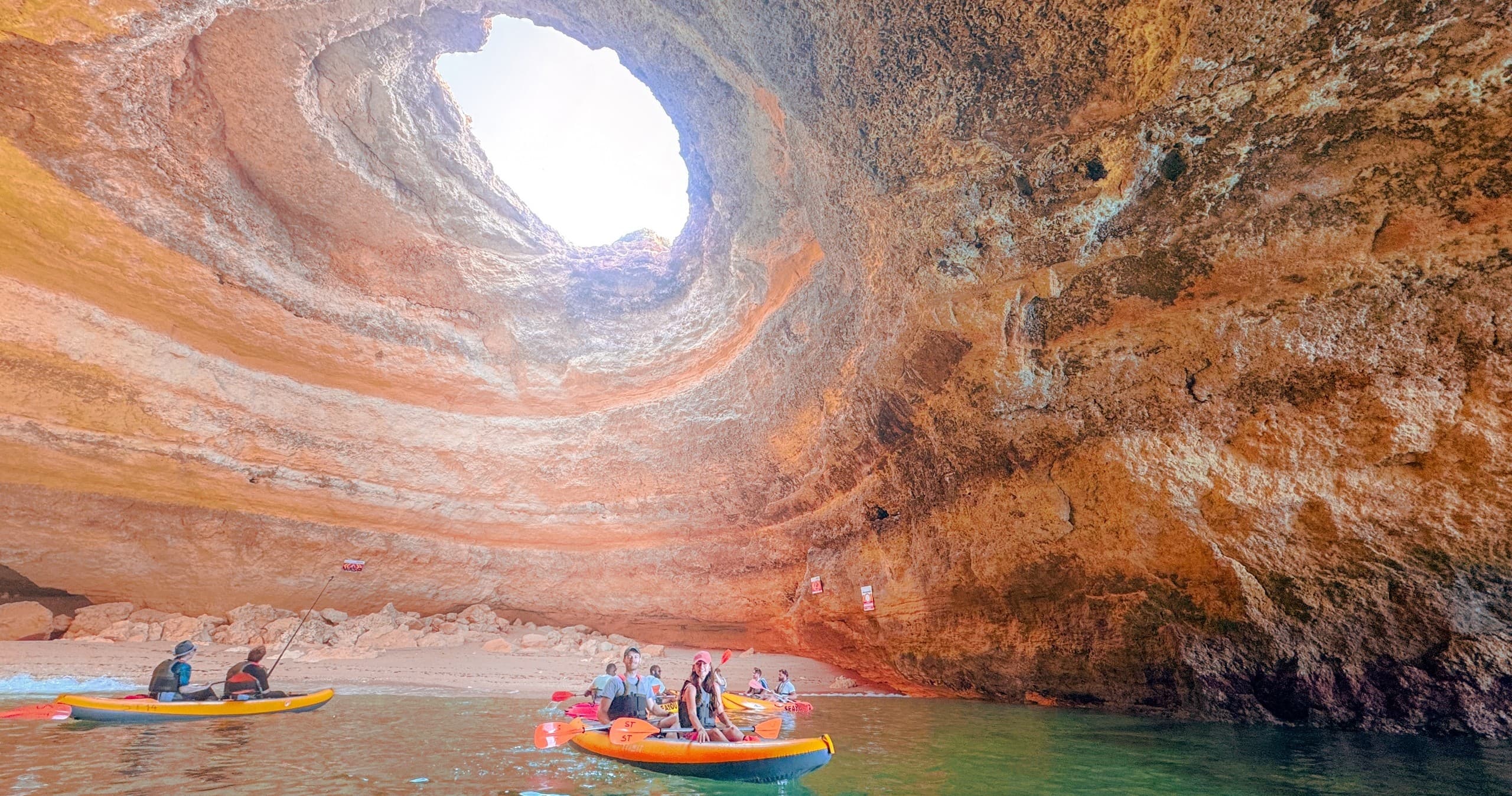 Kayakers paddling inside coastal sea cave with skylight