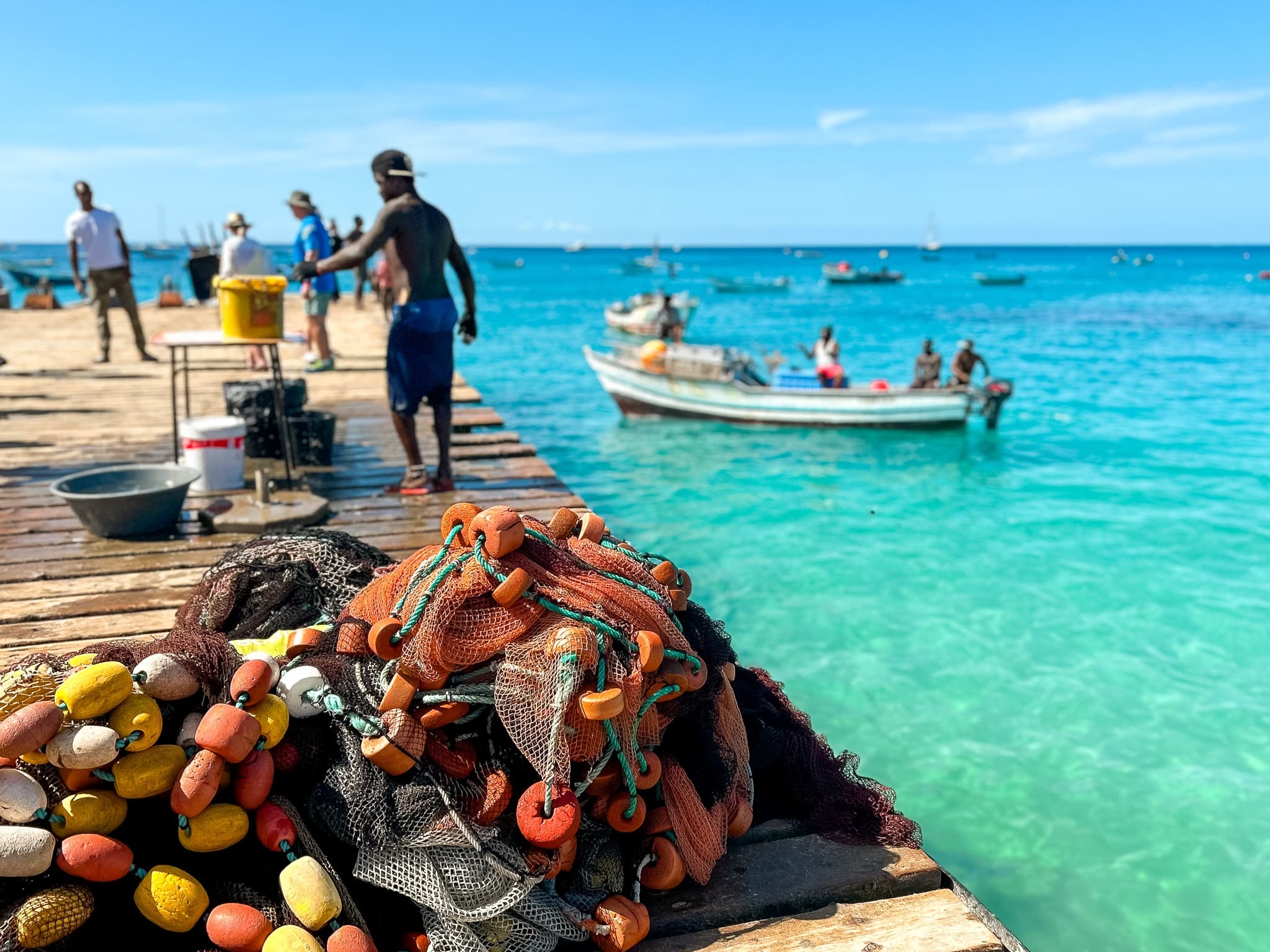 Fishermen unloading nets on sunny pier beside turquoise Caribbean water