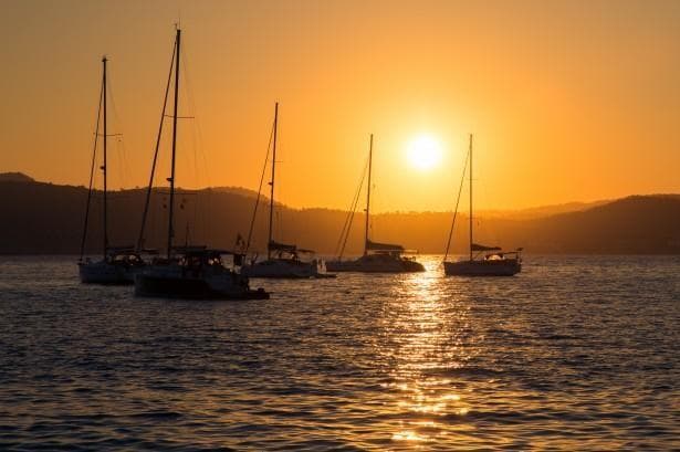 Sailboats anchored at sunset on calm coastal bay