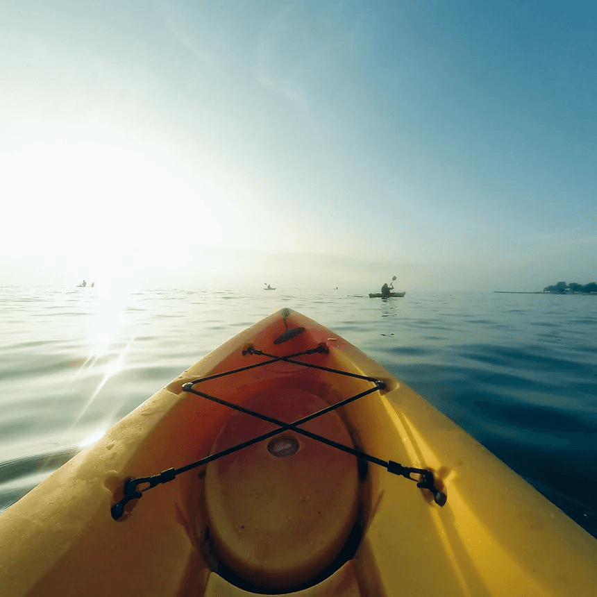 Kayak bow cutting glassy lake at sunrise, paddling on calm water