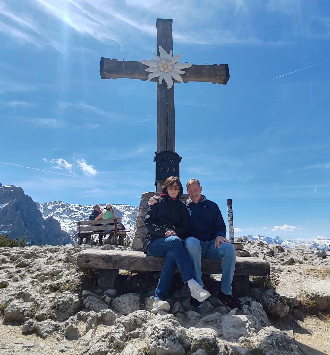 Hikers seated at alpine summit cross with panoramic mountain views