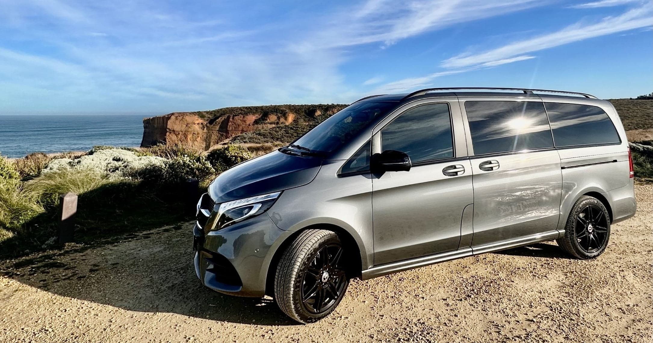 Silver luxury transfer van parked on scenic coastal cliff view
