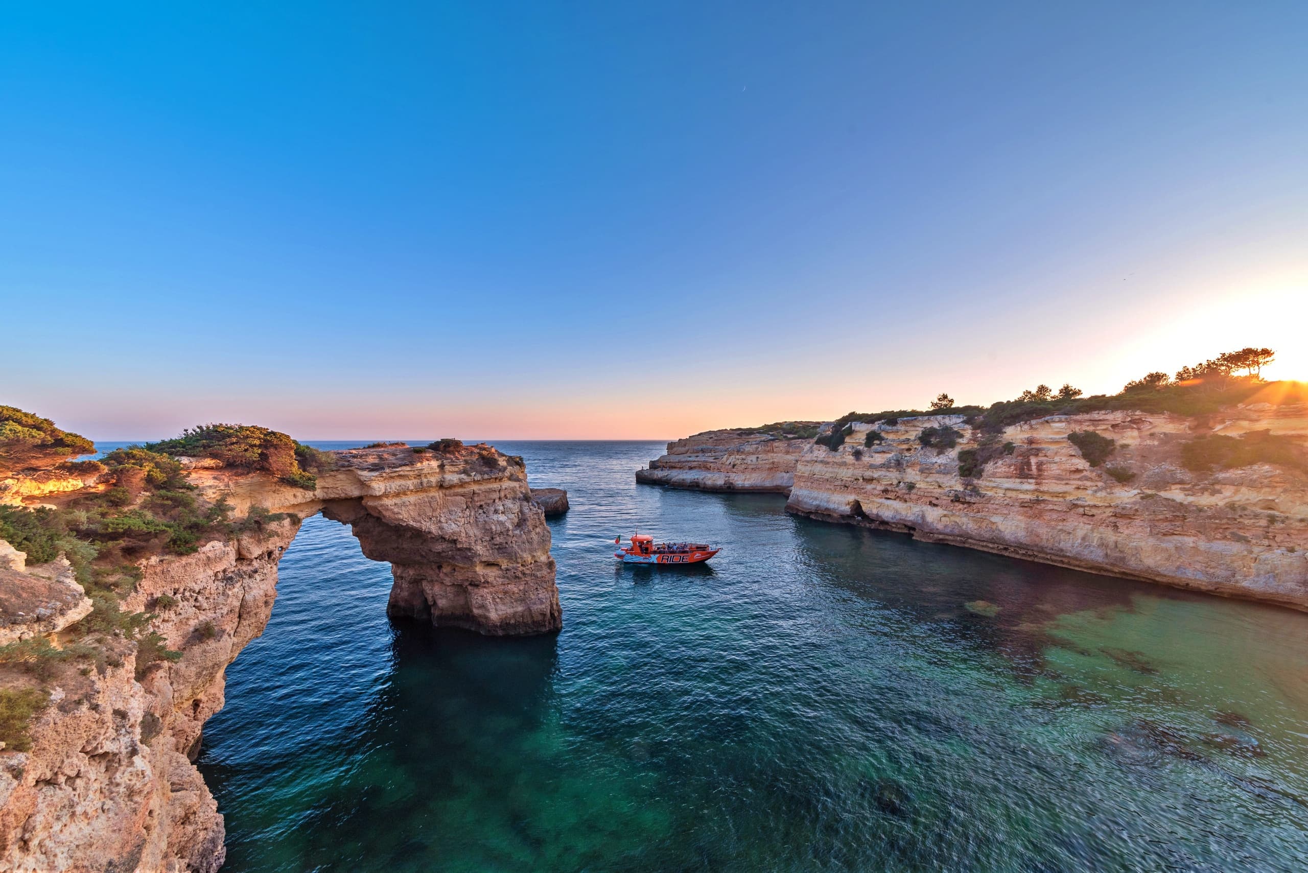 Golden sunset sea arch with small tour boat on Algarve coast