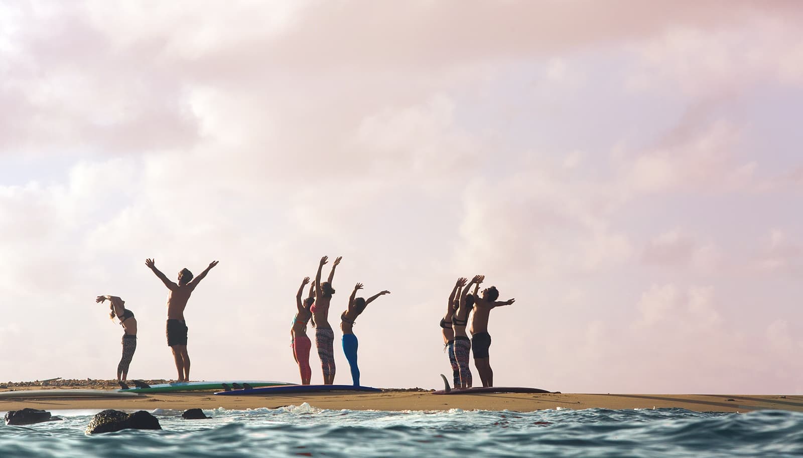 Silhouetted group jumping on rocky shoreline at sunset, ocean view