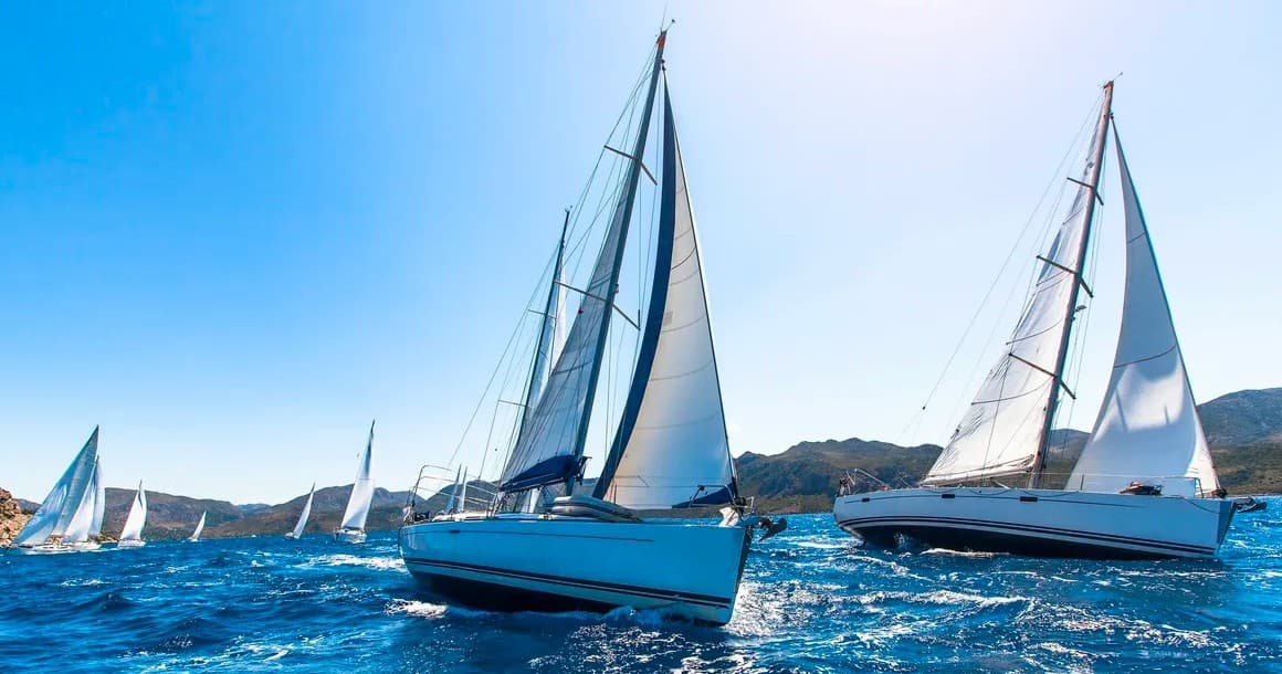 Sailboats racing on open blue sea near coastal shoreline