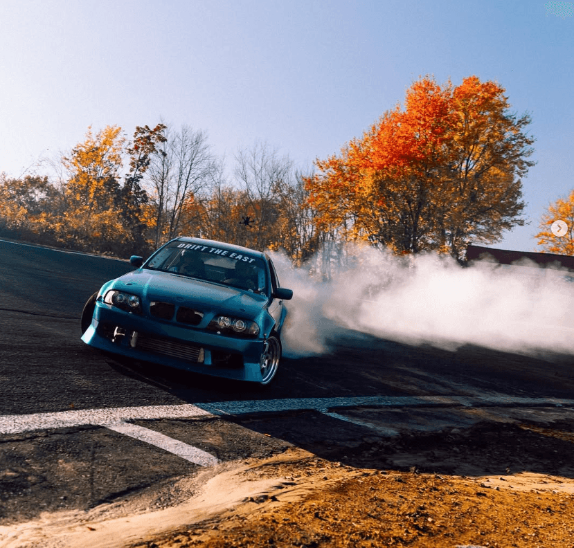 Car drifting on an autumn backroad amid colorful trees and smoke