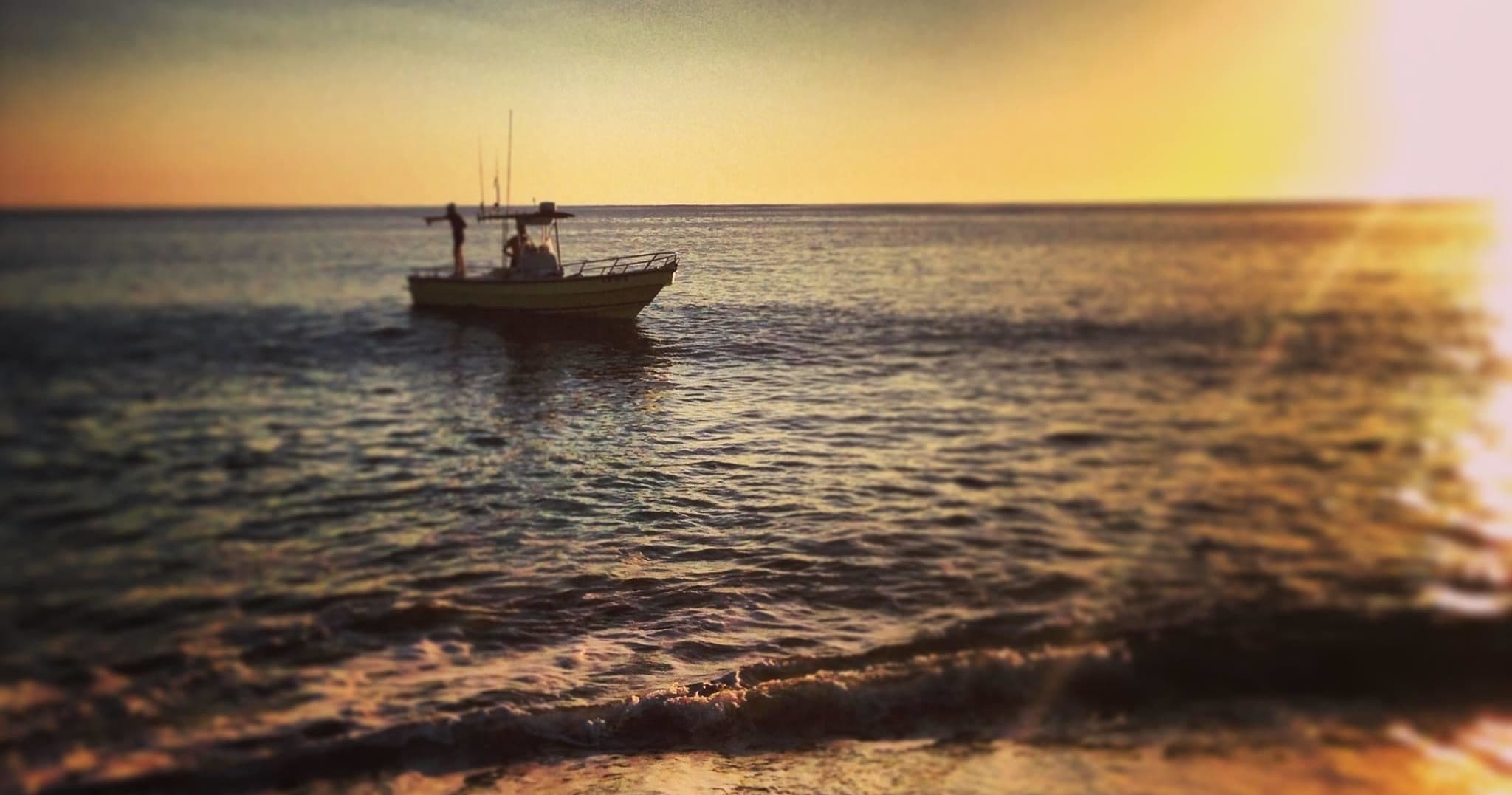 Sportfishing boat silhouetted at sunset over calm ocean waters