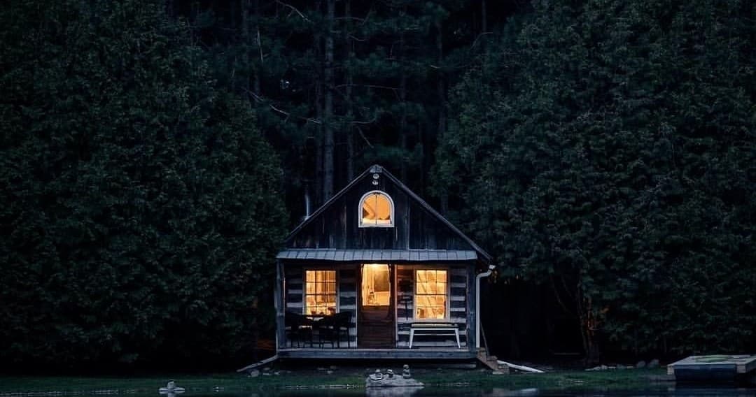 Lakeside wood cabin lit at night, forest retreat with private dock