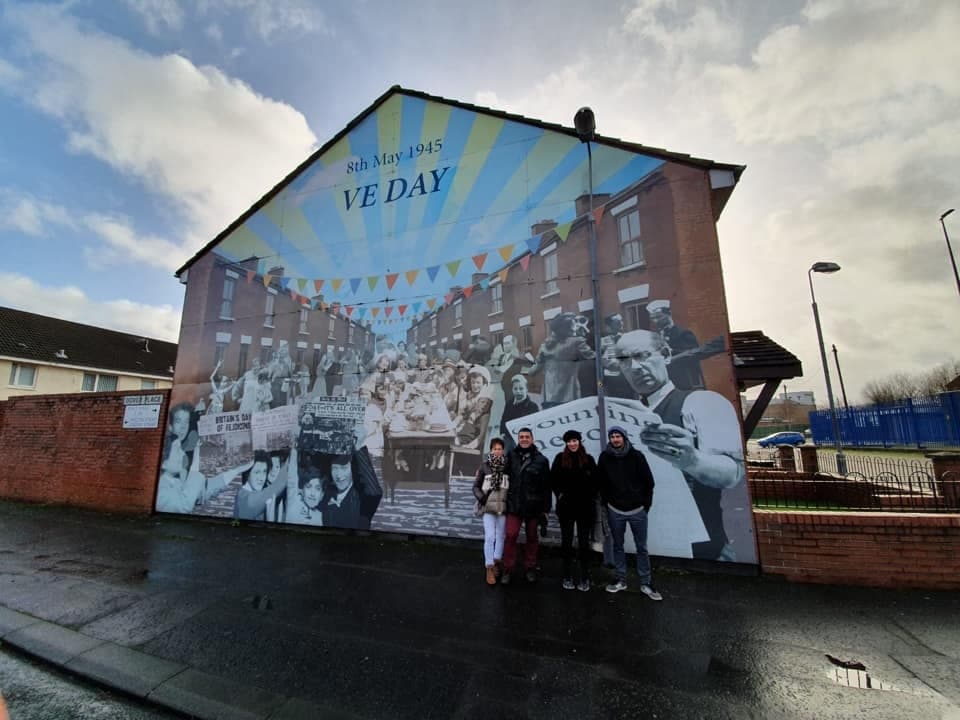 Group posing before large VE Day commemorative mural on Belfast housing