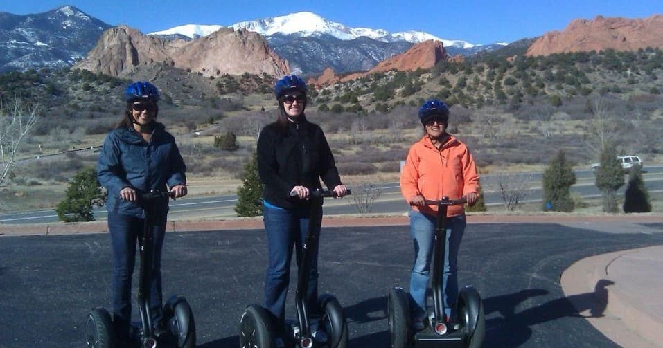 Three people on Segways with red rock formations and snowy peaks