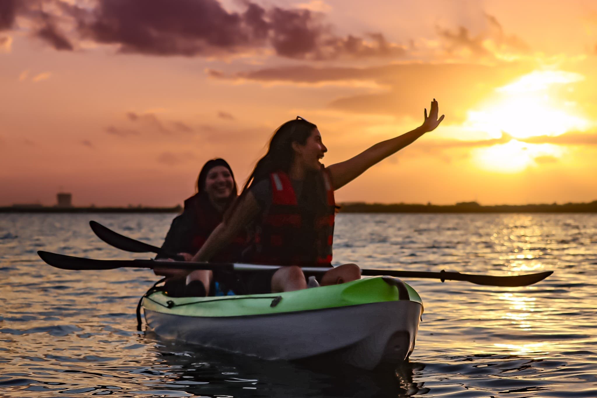 Two kayakers silhouetted paddling at sunset in Cancun waters