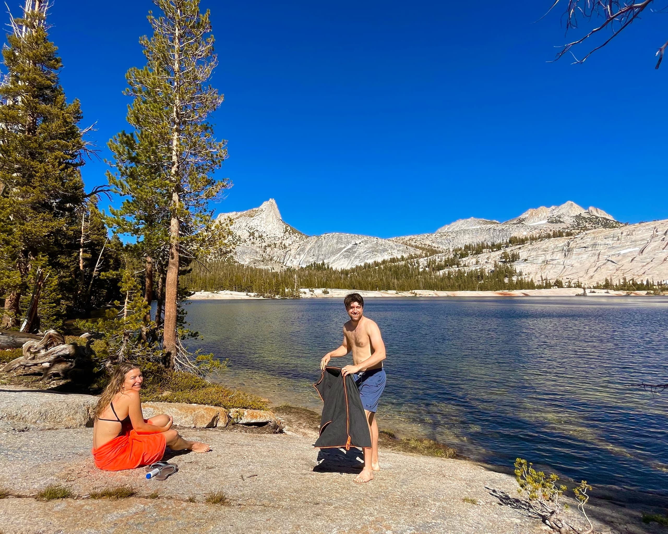 Two hikers relaxing by alpine lake with domed granite backdrop