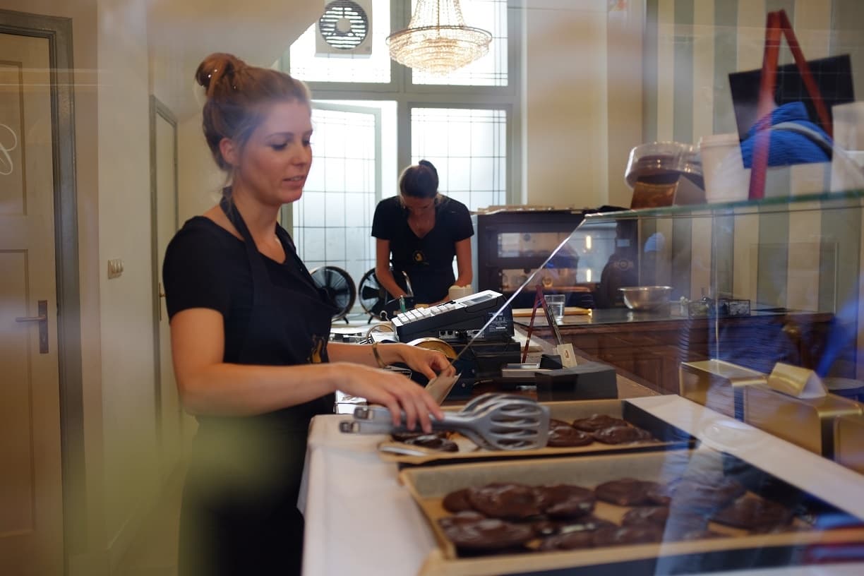 Pastry chef arranging chocolate pastries behind glass in bakery interior
